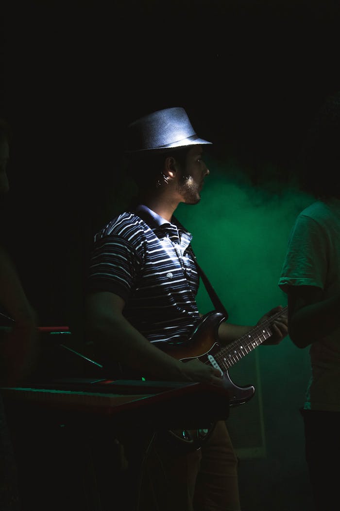 A guitarist in a hat playing live on stage under dramatic lighting.