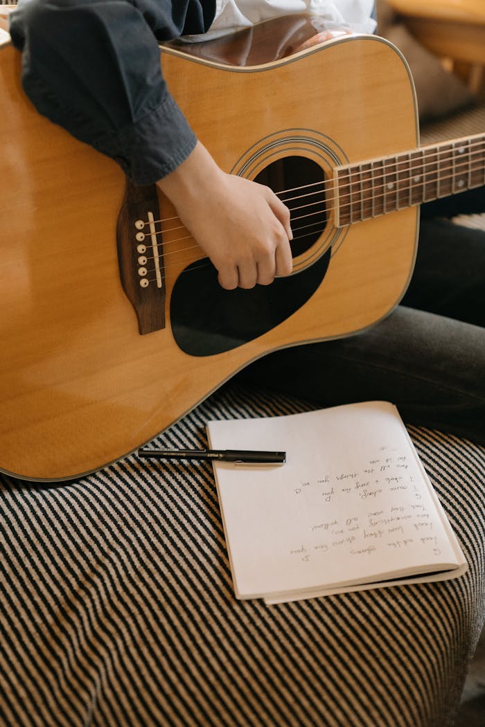 Close-up of a person playing an acoustic guitar with handwritten lyrics nearby.