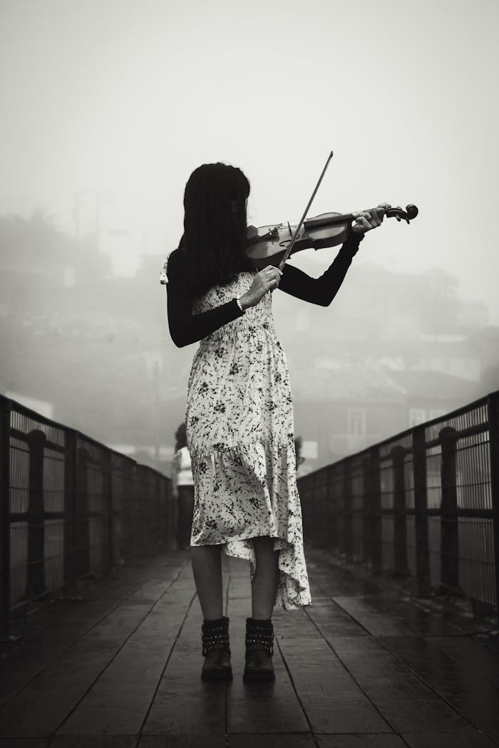 A woman in a floral dress plays violin on a misty bridge, evoking serene creativity.