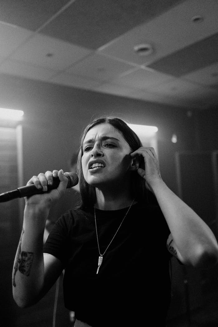 Grayscale close-up of a tattooed singer holding a microphone during a performance.