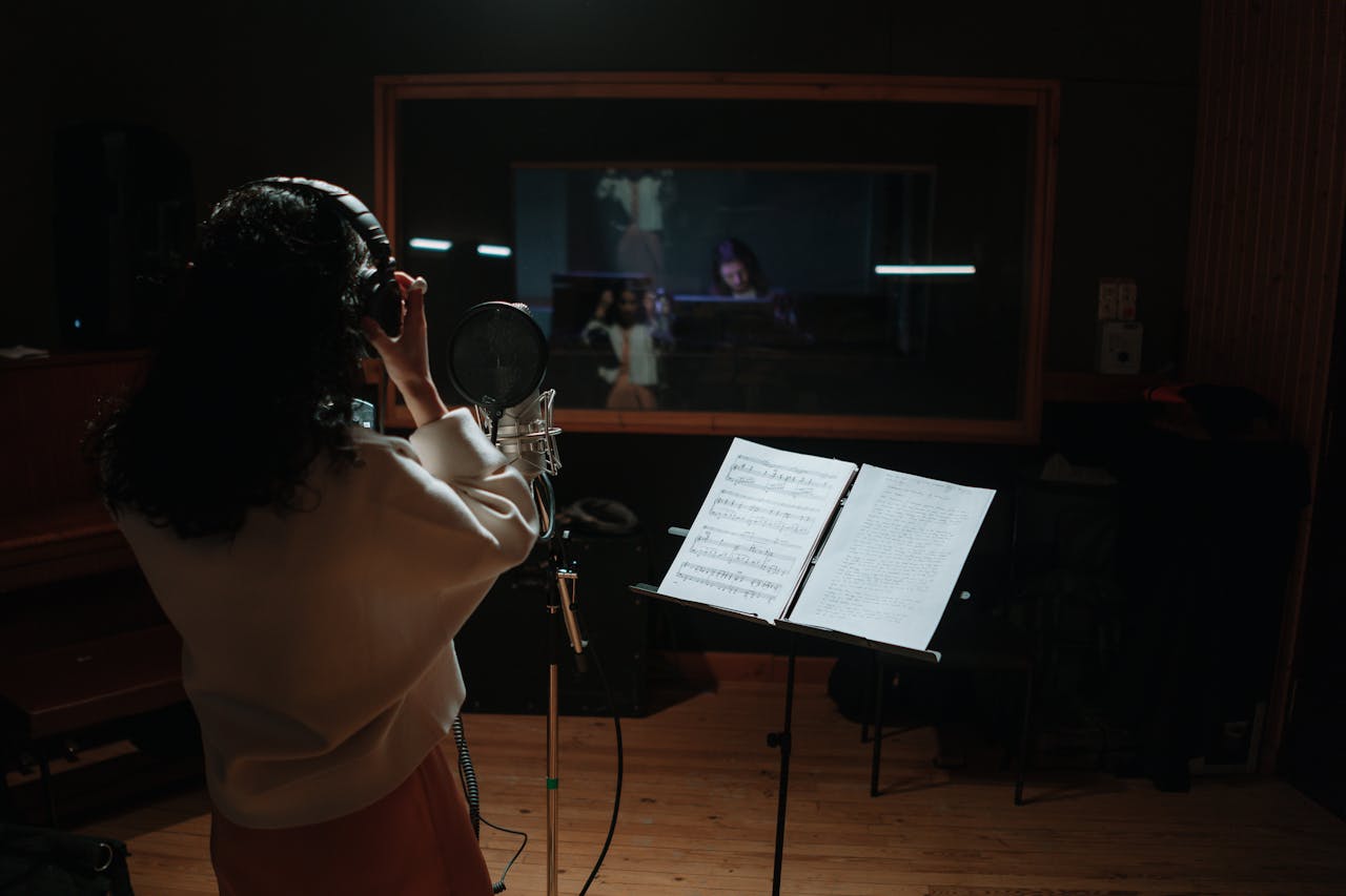 A female singer records vocals in a professional music studio with a microphone and sheet music.