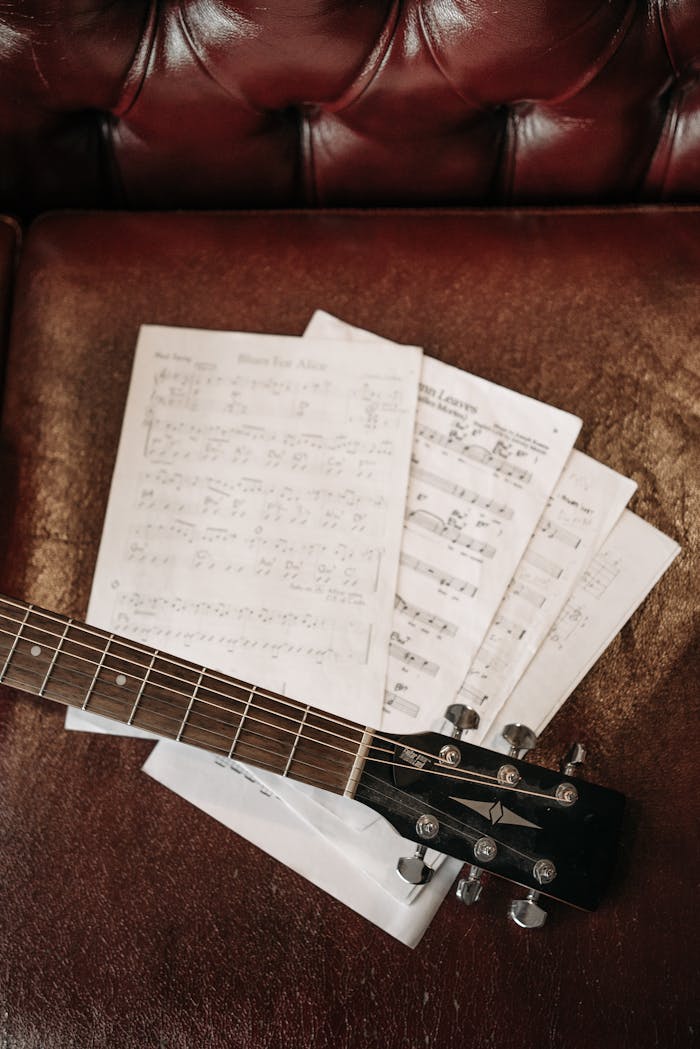Close-up of a guitar neck on a leather sofa, displaying sheet music.